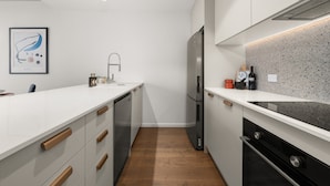 A modern kitchen with white cabinetry, stainless steel appliances, and a speckled backsplash. - Chic and Elegant 1-bed in Unbeatable Location (Canberra)