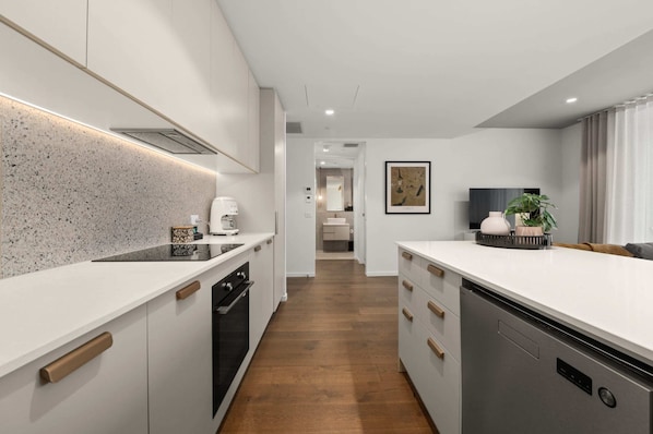 A modern kitchen with white cabinetry, a speckled backsplash, and a central island. - Chic and Elegant 1-bed in Unbeatable Location (Canberra)