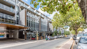 A modern building with a glass facade, a low clearance sign, and a 'Daballo' sign indicating a nearby restaurant. - Chic and Elegant 1-bed in Unbeatable Location (Canberra)