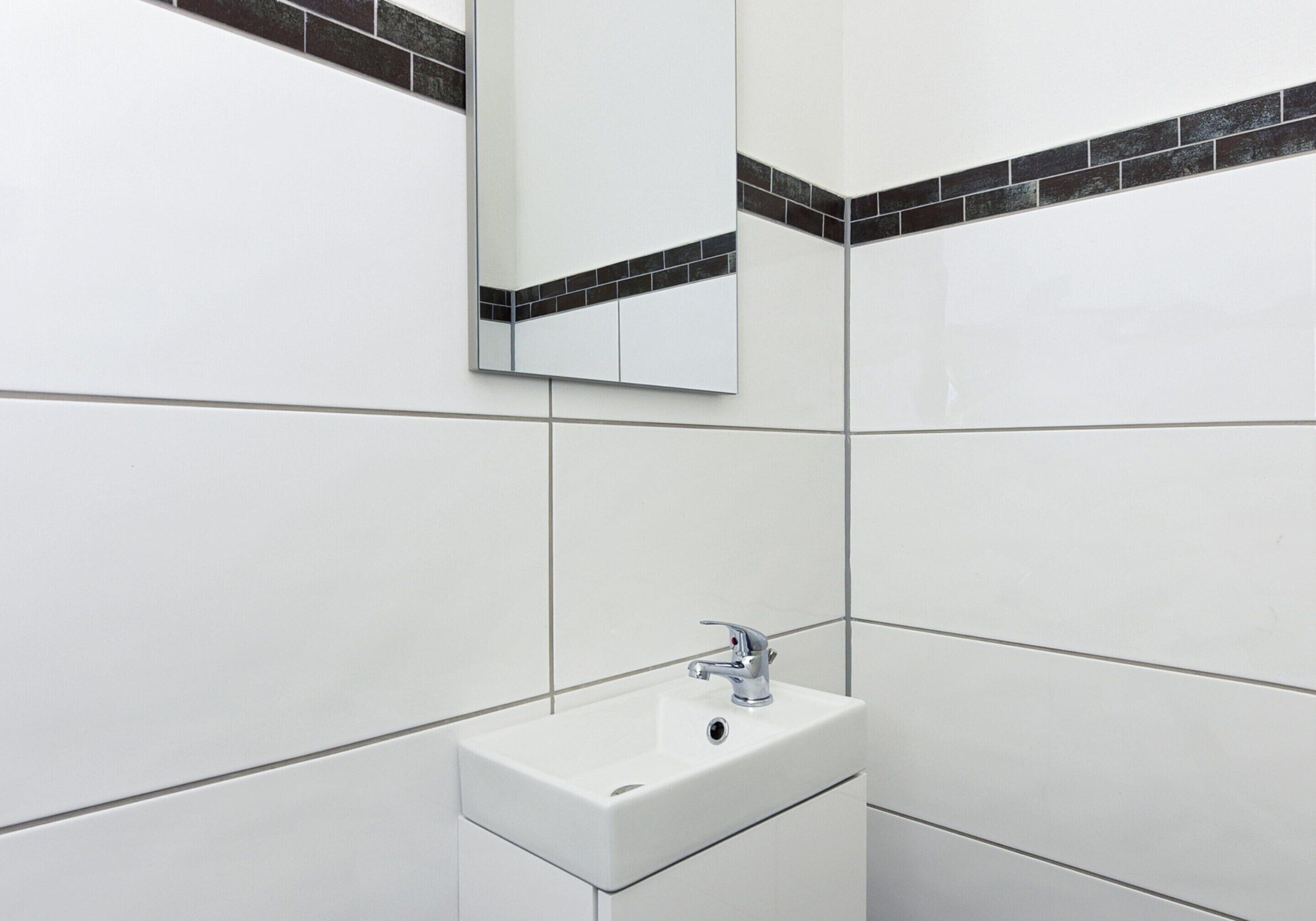 Ein Badezimmer mit einem weißen Waschbecken, einem Spiegel und schwarzen Fliesenwänden.