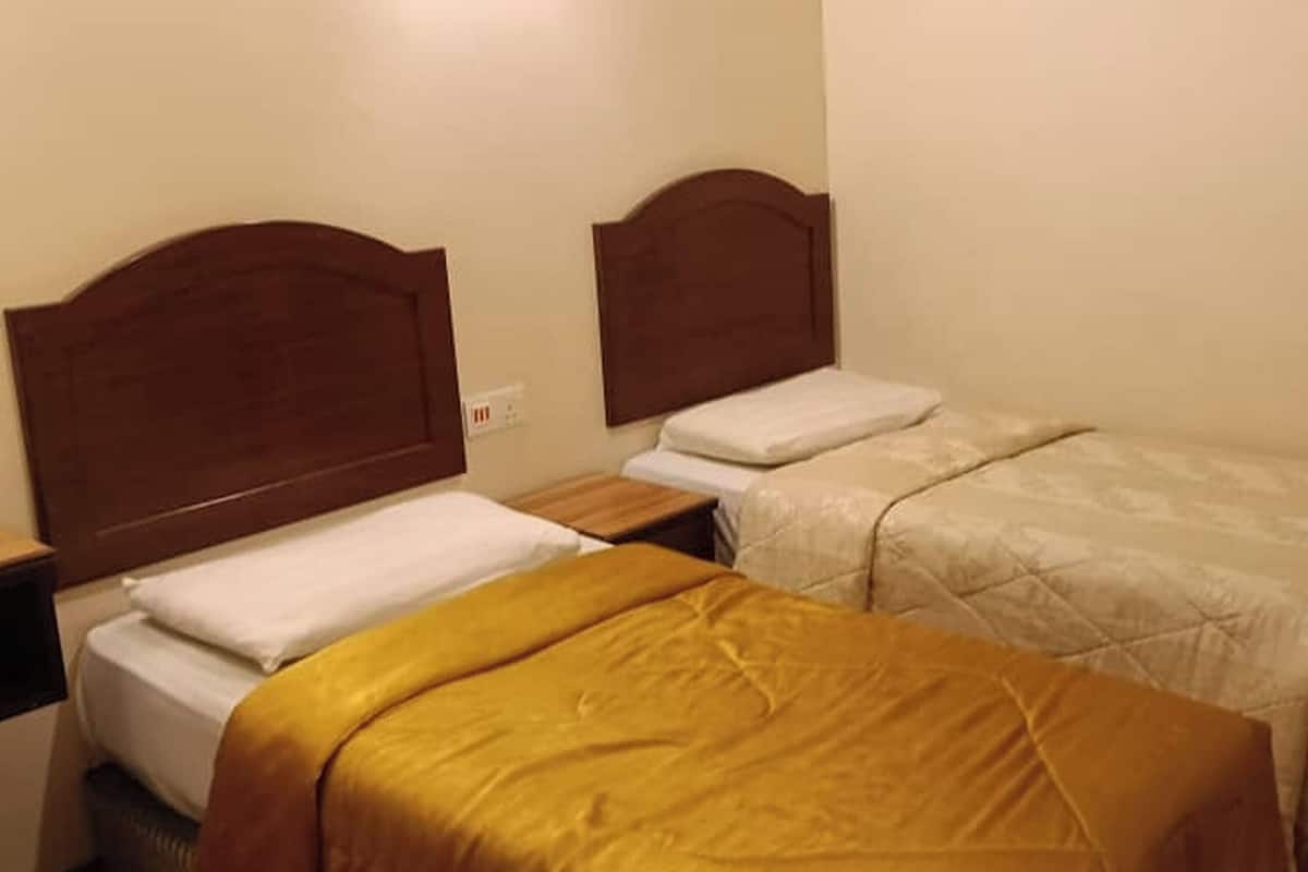 Ein Hotelzimmer mit zwei Einzelbetten, Holz-Kopfteilen und einem Nachttisch mit Lampe.