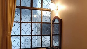 A room with a large window featuring a geometric pattern, a small table with a kettle and water bottles, and a wall-mounted mirror. - Hotel Remix 2 Cameron Highlands (Brinchang)
