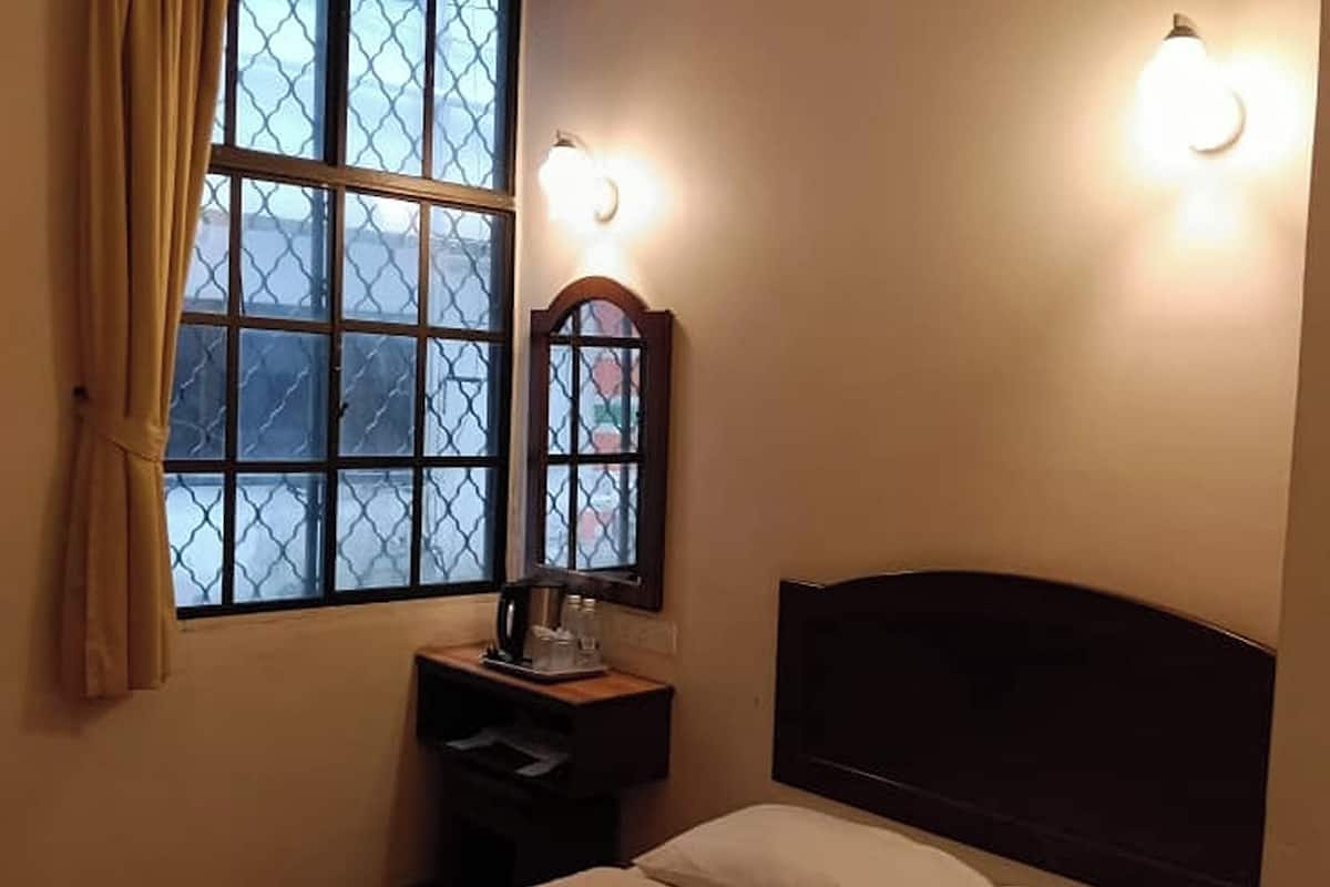 Ein Schlafzimmer mit einem Bett, einem Nachttisch, einem Fenster mit Vorhängen und Wandleuchten.