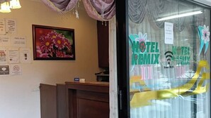 A hotel reception area with a desk, a framed floral artwork, and a window displaying the hotel's name and amenities. - Hotel Remix 2 Cameron Highlands (Brinchang)