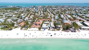 Vista aérea de una zona residencial costera con propiedades frente a la playa, una playa de arena y aguas turquesas cristalinas.