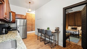A modern kitchen with a stainless steel refrigerator, wooden cabinets, and a granite countertop. There are three bar stools and a small table with a plant. - Stable #1 ~Walkable, BBQ, Fire Pits, Mini Golf (Louisville)