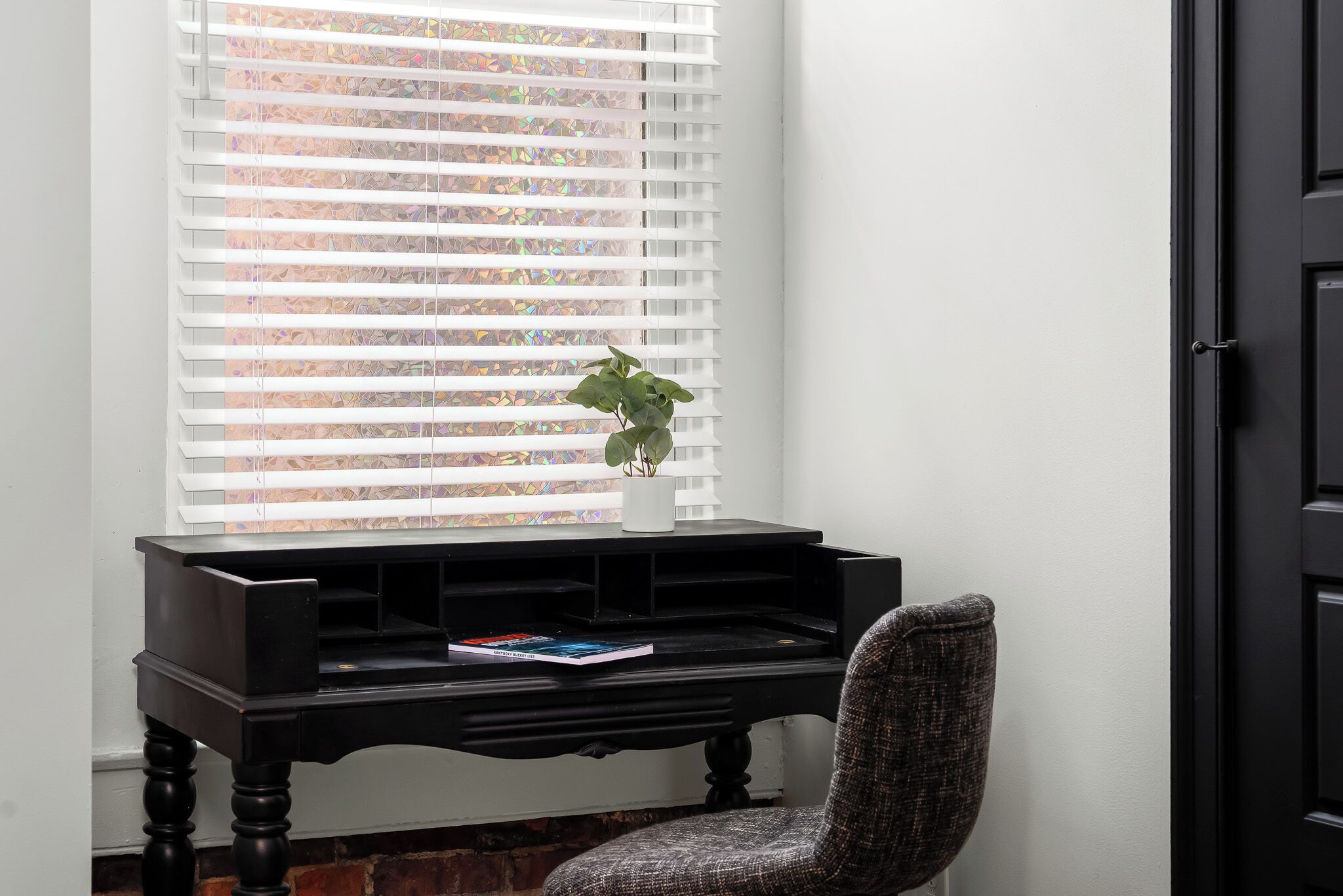 Une pièce d’angle avec un banc de piano noir, une chaise et une fenêtre avec des stores.