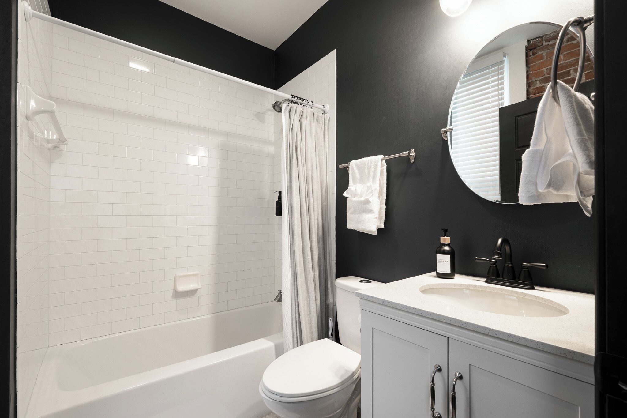 Une salle de bain moderne avec une baignoire blanche, des toilettes, un lavabo avec un miroir et un rideau de douche.