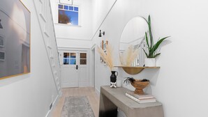 A hallway with a grey rug, a console table with books and a vase, a mirror, and a potted plant. - Charming 4-Bedroom Home in Peaceful Parkside Setting with Hot Tub & Sauna (North Vancouver)