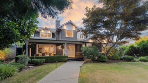 A two-story house with a paved driveway leading to the front door, surrounded by well-maintained lawns and various shrubs. - Charming 4-Bedroom Home in Peaceful Parkside Setting with Hot Tub & Sauna (North Vancouver)