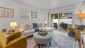 A living room with a sofa, two armchairs, a coffee table, and a patterned rug. There is a window with blinds, a lamp, and a framed picture on the wall. - Ground Level Condo by Sunset High School (Portland)