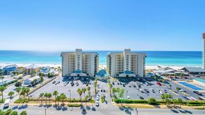 A hotel with a parking lot, a beach view, and a tall building in the background. - Laketown Wharf 1213 (Panama City Beach)