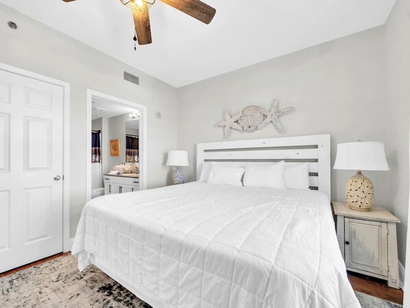 A bedroom with a large bed, white walls, a ceiling fan, and a decorative starfish on the wall. - Laketown Wharf 1213 (Panama City Beach)