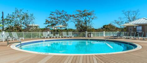 A wooden deck with a pool, lounge chairs, and a fenced area.