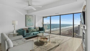 A modern living room with a large window offering a view of the beach. - Forest Dunes 1802- Ocean View 3BR/2.5BA- Pool (Myrtle Beach)