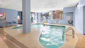An indoor swimming pool with clear water, a lifeguard duty sign, and a view of the outside through large windows. - Forest Dunes 1802- Ocean View 3BR/2.5BA- Pool (Myrtle Beach)