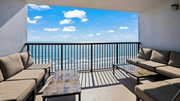 A balcony with a view of the sea, furnished with sofas and a table. - Regency Towers 907- Oceanfront 3BR- Pool (Myrtle Beach)
