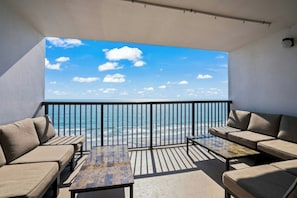 A balcony with a view of the sea, furnished with sofas and a table. - Regency Towers 907- Oceanfront 3BR- Pool (Myrtle Beach)