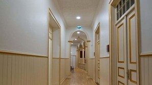Un corridoio con pavimento in legno, pareti bianche e porte con modanature dorate.