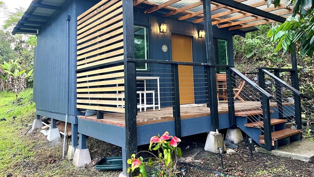A small, blue wooden cabin with a wooden deck and a covered porch. - Charming cabin in Pāhoa for a peaceful getaway (Pāhoa)