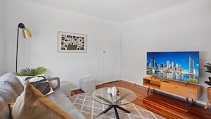 A modern living room with a sofa, a glass coffee table, a flat-screen TV, and a cityscape painting. - Windsor Cosy 2-bedroom Unit in Quiet Neighborhood (Brisbane)