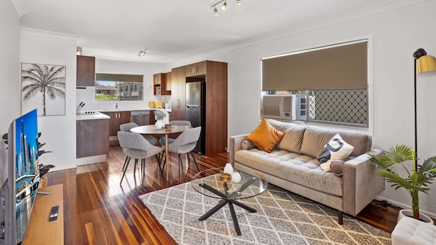 A modern living room with a sofa, coffee table, and dining area. - Windsor Cosy 2-bedroom Unit in Quiet Neighborhood (Brisbane)