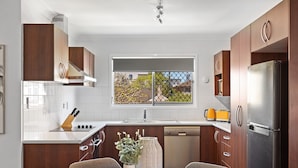 A modern kitchen with wooden cabinets, a stainless steel refrigerator, and a dining area with a table and chairs. - Windsor Cosy 2-bedroom Unit in Quiet Neighborhood (Brisbane)