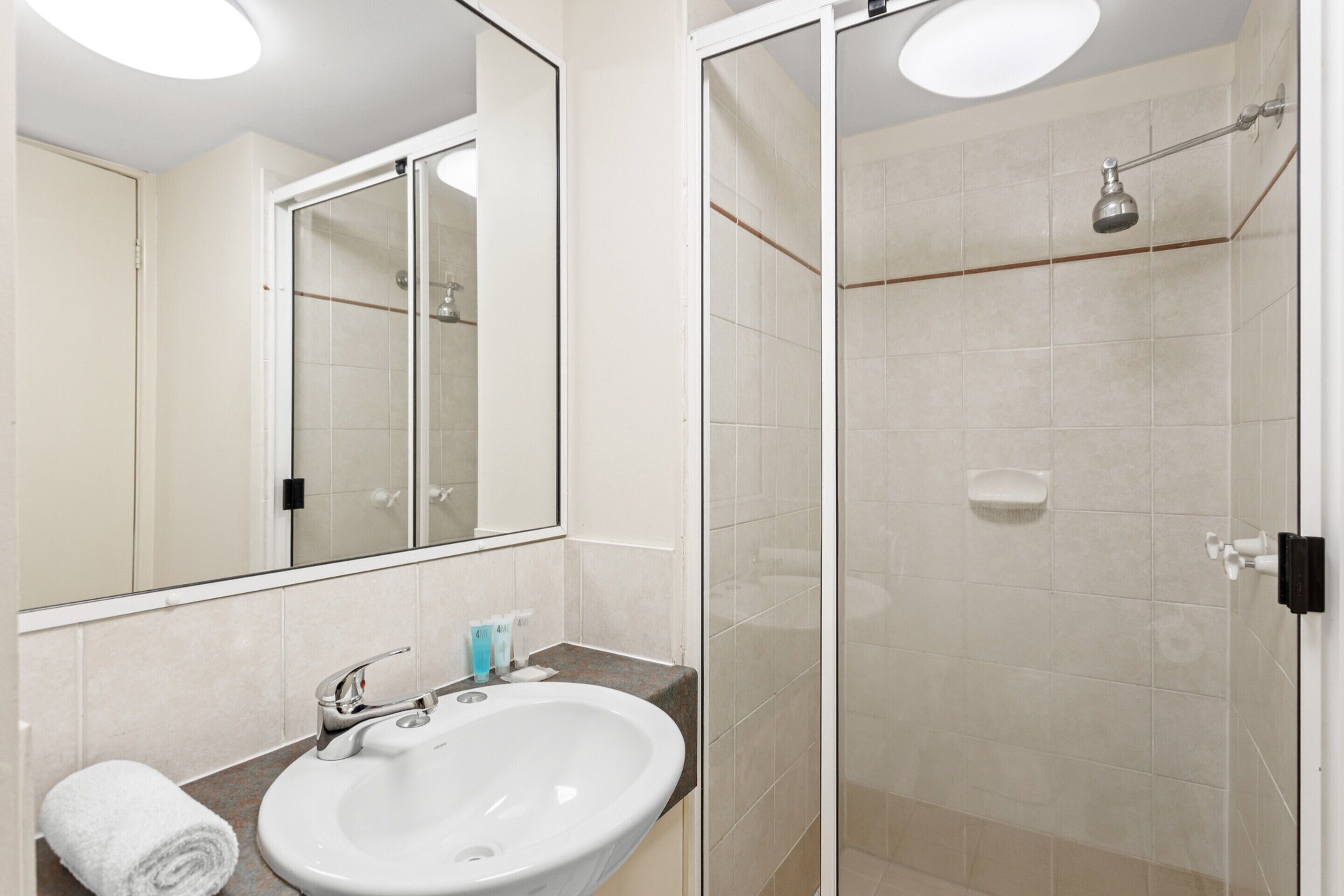 Un baño con lavamanos blanco, espejo y cabina de ducha con mampara de vidrio.