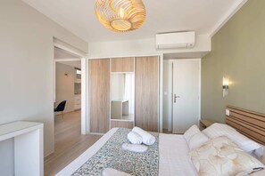 A modern hotel room with a bed, a wooden wardrobe, a bathroom, and a hallway leading to another room.