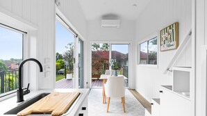 Eine moderne Küche mit großem Fenster, einem Holzbruchbrett und einem weißen Essbereich mit Tisch und Stühlen.