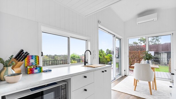 Eine moderne Küche mit einer großen Kochinsel, weißen Schränken und Blick in den Garten durch große Fenster.