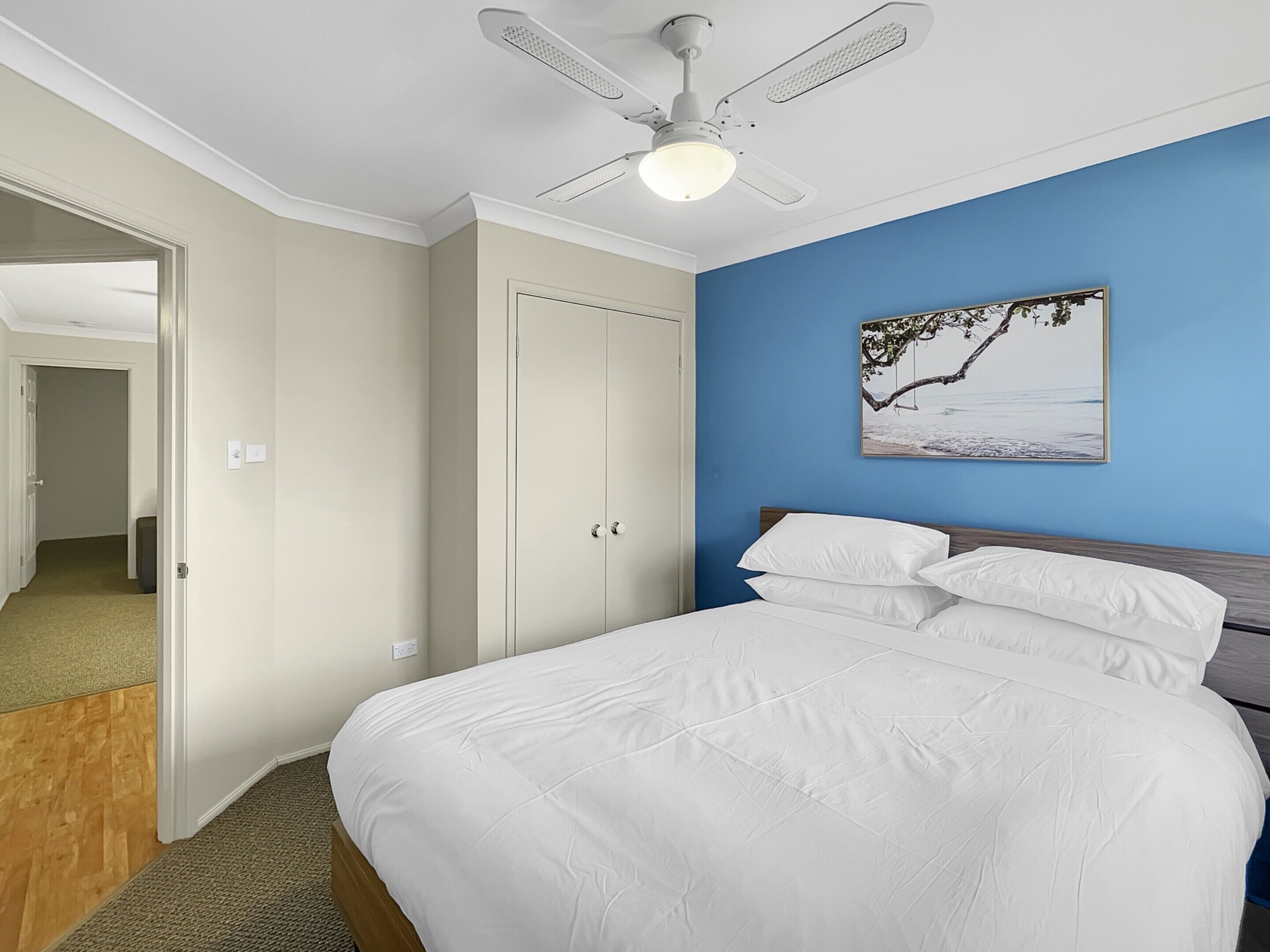 A bedroom with a bed, a ceiling fan, a door, and a wall with a picture.