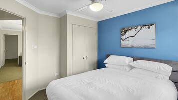 A bedroom with a bed, a ceiling fan, a door, and a wall with a picture.