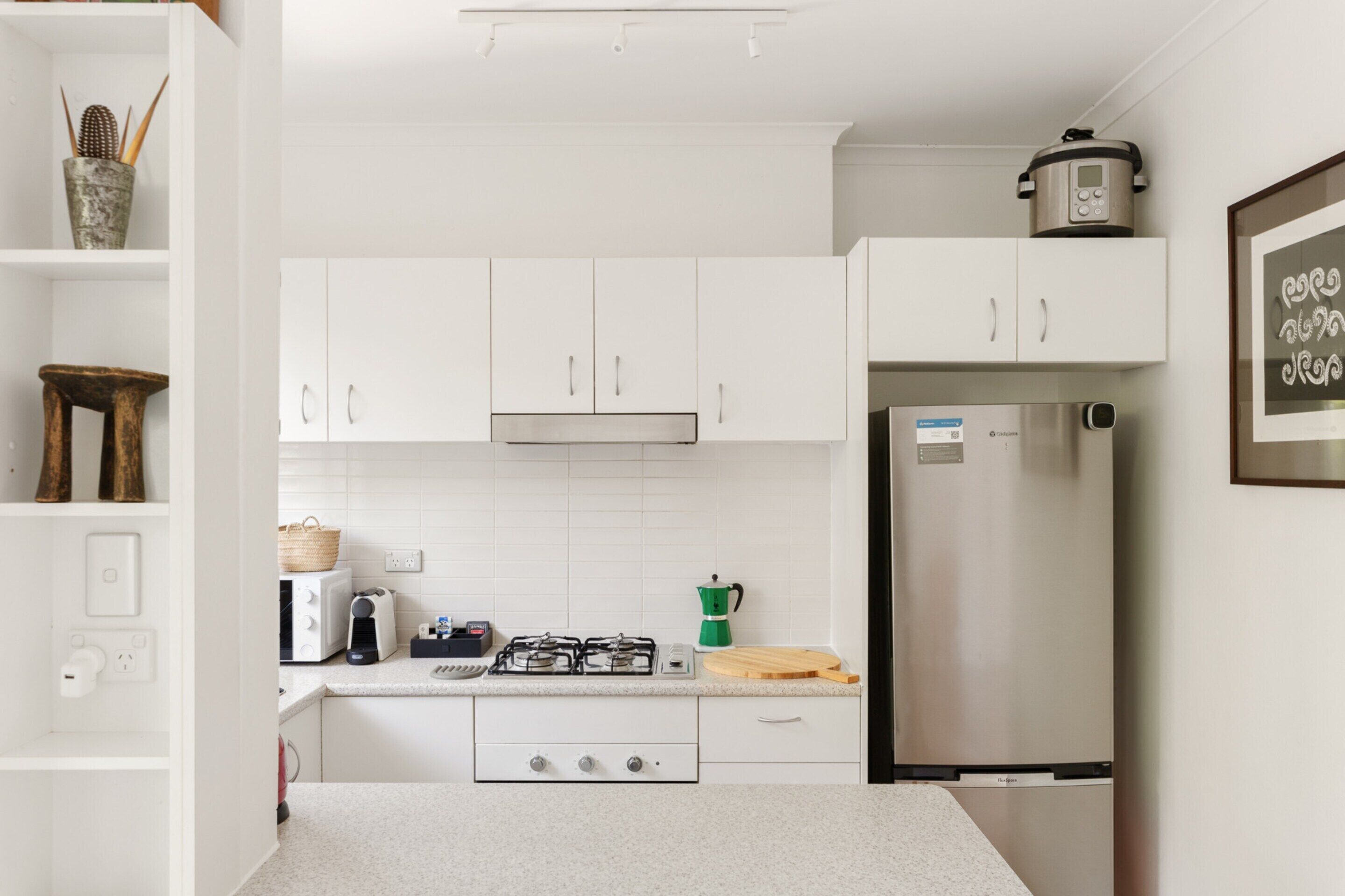 A modern kitchen with white cabinets, a stainless steel refrigerator, a gas stove, and a coffee maker.