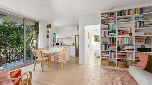 A modern kitchen with white cabinets, a dining area with wooden chairs, and a large bookshelf filled with books.
