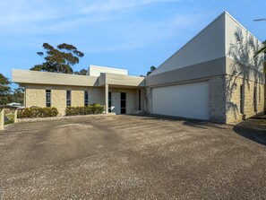 Um edifício moderno de dois andares com garagem, entrada de automóveis em cascalho e um jardim frontal ajardinado.