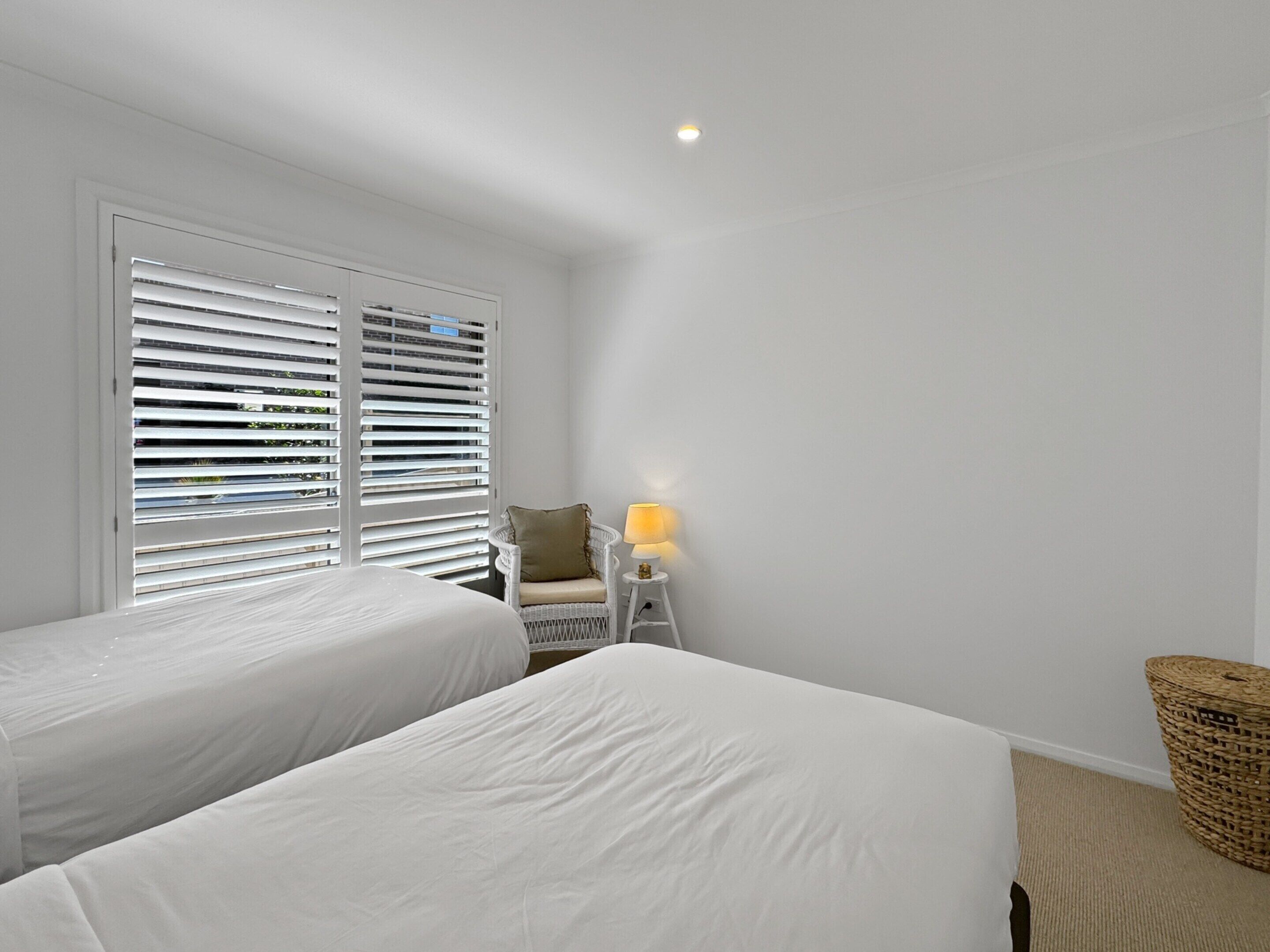 Une chambre avec deux lits, une chaise, une lampe et une fenêtre avec des stores.