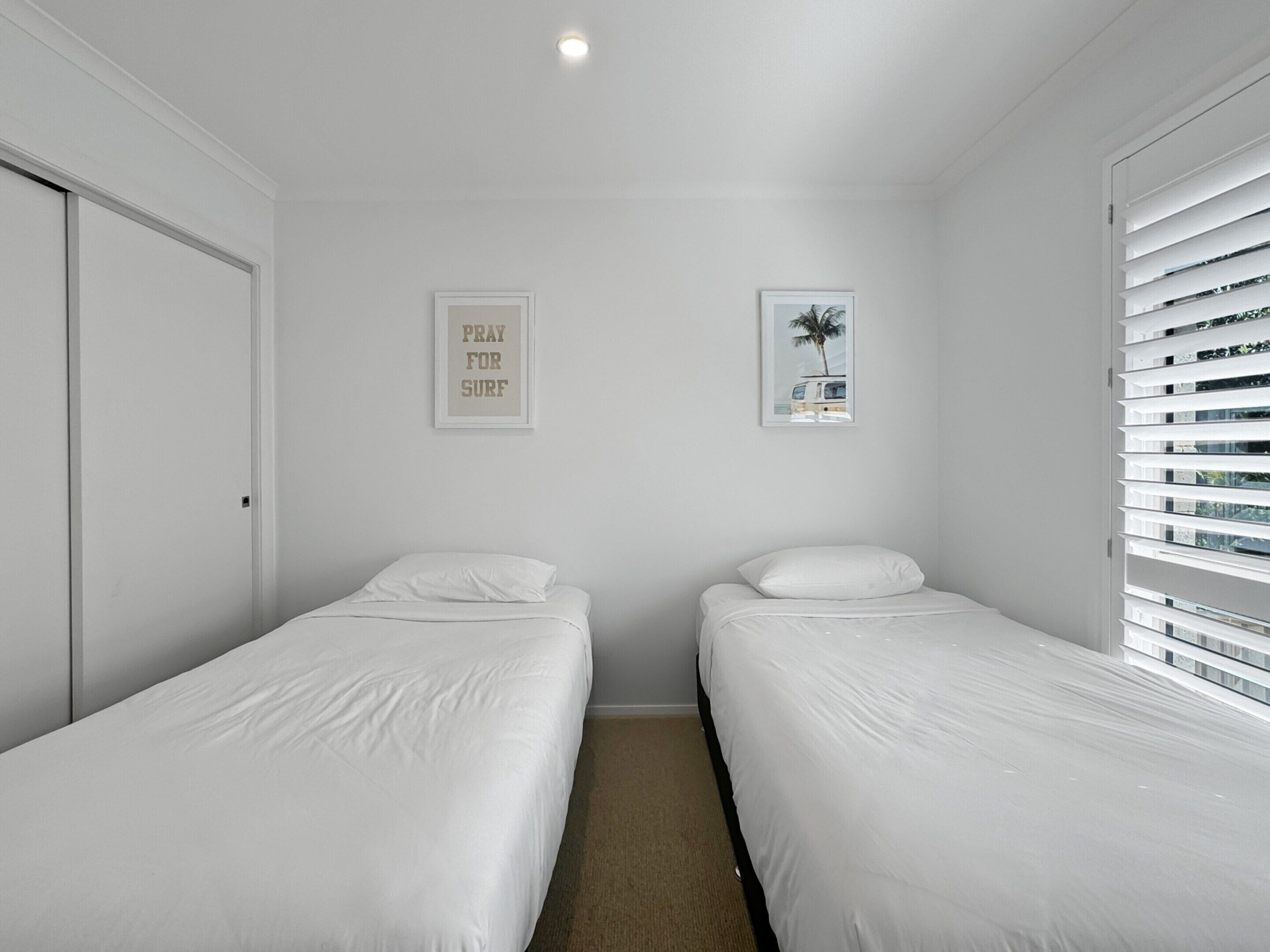 Une petite chambre propre, avec deux lits simples, une porte et deux tableaux encadrés accrochés aux murs.