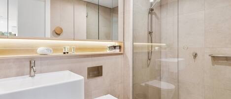 Un baño moderno con ducha de vidrio, lavamanos blanco y retrete.
