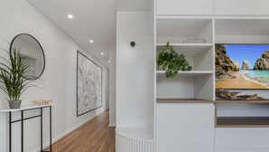 Un interior moderno con suelo de madera, una consola blanca con planta en maceta, una obra de arte enmarcada y una estantería con una escena de playa.