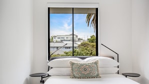 Un dormitorio con cama, ventana y vista a edificios.