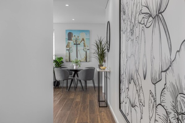 A modern dining area with a wooden floor, grey chairs, a small round table, and a potted plant. - North-east Facing Modern 2-bed Apartment (Sydney)