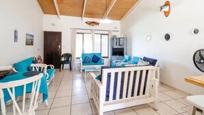 A spacious living area with a high ceiling, a wooden ceiling, a white sofa with blue cushions, a white table, and a white chair. - CASA DEL SOL 4 a Stroll to the beach (Margate)