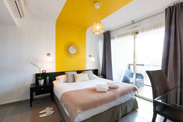 Habitación de hotel moderna con una cama grande, una mesita de noche, una silla y vistas a la ciudad a través del ventanal.