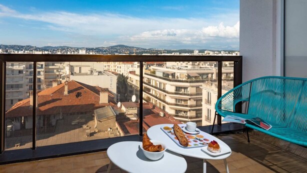 A balcony with a table set for breakfast, a chair, and a view of the cityscape. - One-bedroom Terrace 7A (Antibes)