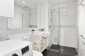 A modern bathroom with a glass-enclosed shower, a white sink, and a built-in washing machine. - Stylish Southbank 2-bed Flat w/ Balcony (Melbourne)