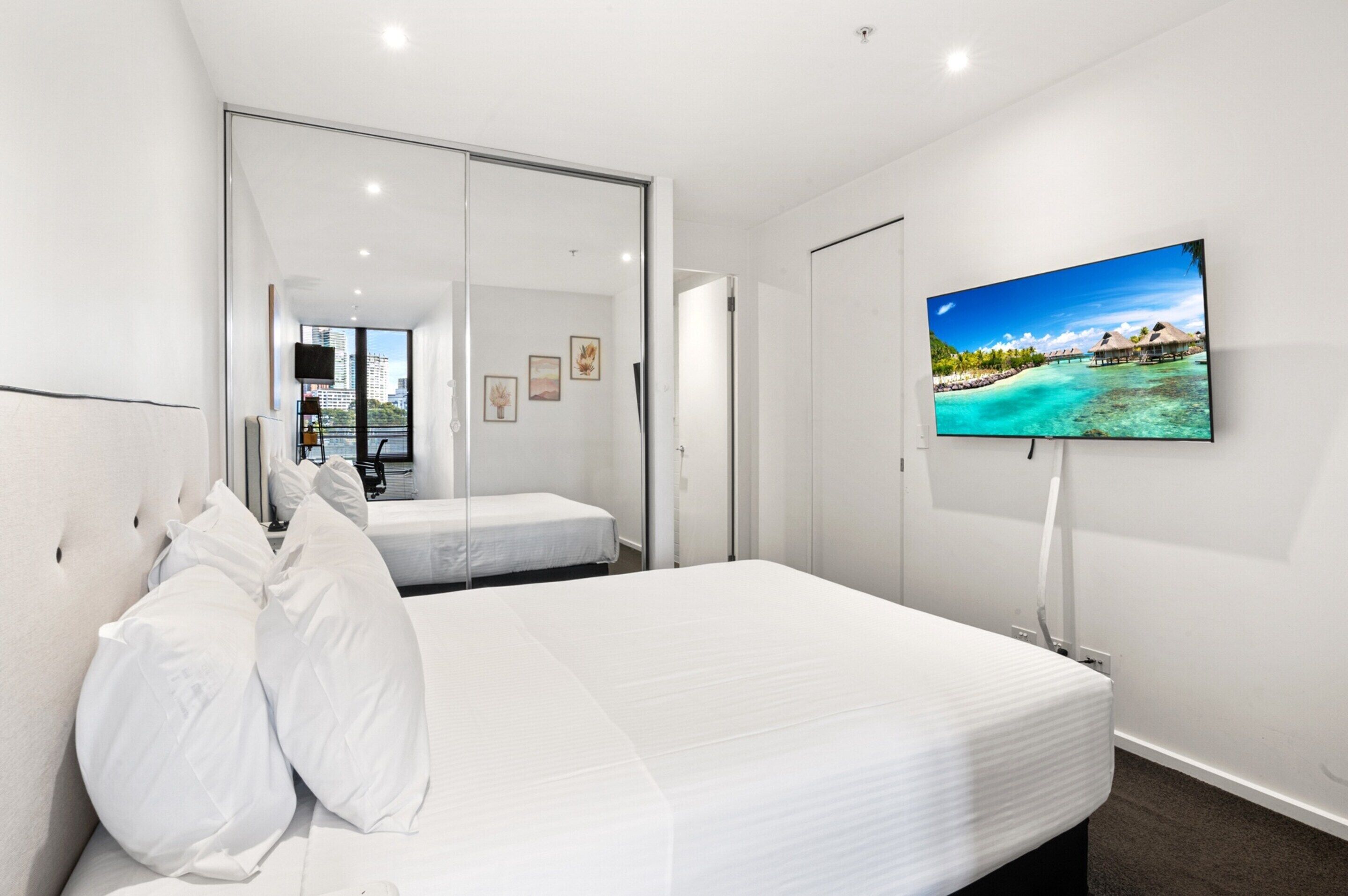 Ein Schlafzimmer mit einem Bett, einem an der Wand montierten Fernseher und einer Schiebetür, die auf einen Balkon führt.