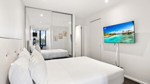 A bedroom with a bed, a television mounted on the wall, and a sliding door leading to a balcony.
