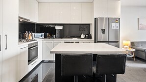 A modern kitchen with white cabinets, a central island, a refrigerator, and a microwave.