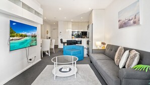 A modern living room with a flat-screen TV, a grey sofa, a blue armchair, and a glass coffee table.